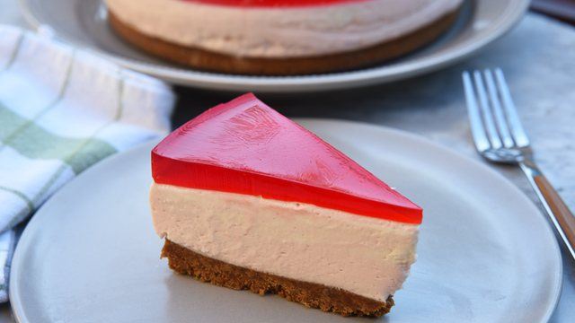 slice of a layered strawberry cheesecake with strawberry jelly topping on a white plate