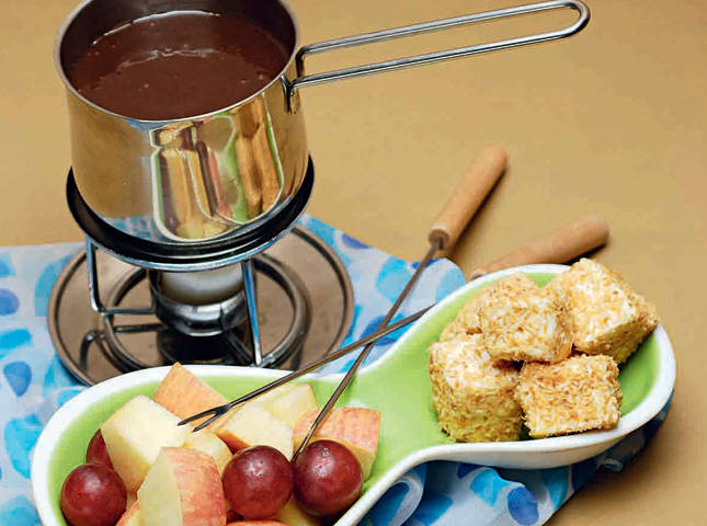 apples, grapes and marshmallows on an abstract plate with fondue sticks, with wine chocolate fondue in a fondue warmer 