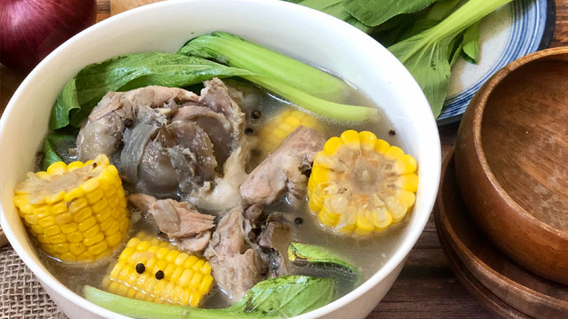 pork bulalo in a white bowl, surrounded by a wooden bowl, a plate of bok choy and onions