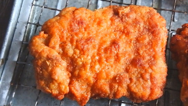 crispy fried chicken thigh fillet on a cooling rack after frying 