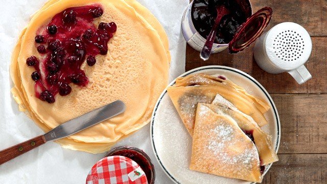left: crepe being filled with blueberry preserves. right: crepes already filled, folded and stacked