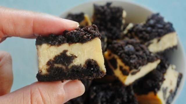 Oreo cheesecake cubes in a bowl, with one cube being held in the foreground