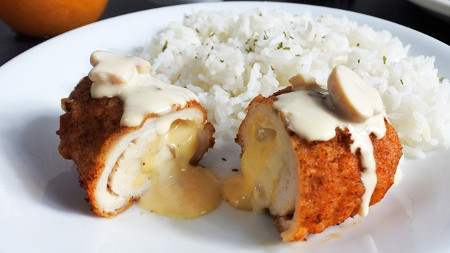 chicken cordon bleu sliced in half with cheese and creamy mushroom oozing out on a plate with rice