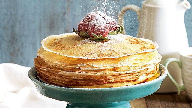 crepe cake topped with strawberries with powdered sugar being sprinkled on top
