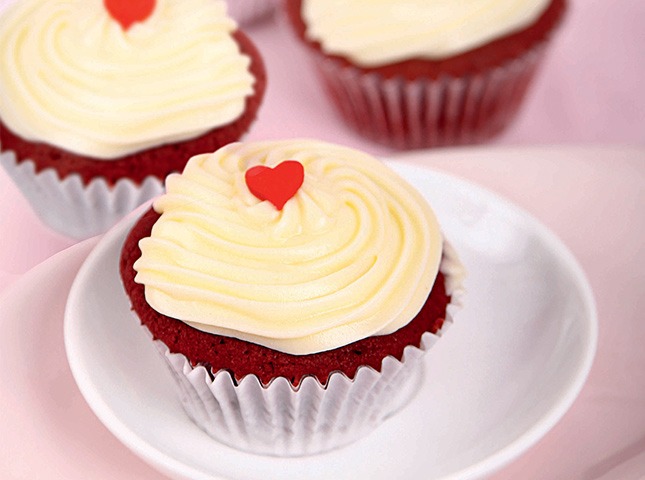 Red velvet cupcakes topped with a heart sprinkle on a white plate