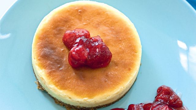 classic cheesecake topped with macerated strawberries on a blue plate